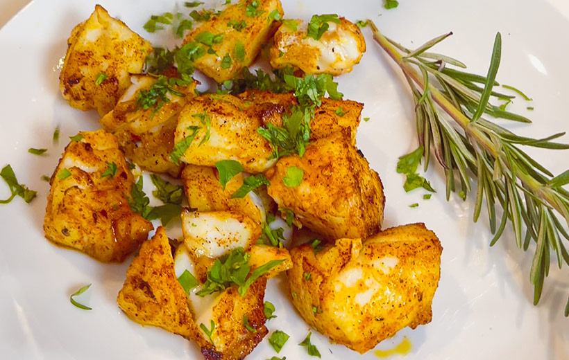 Fish bites, pan-seared with mediterranean spice blend "Grill-Thrill". On a plate garnished with chopped herbs.