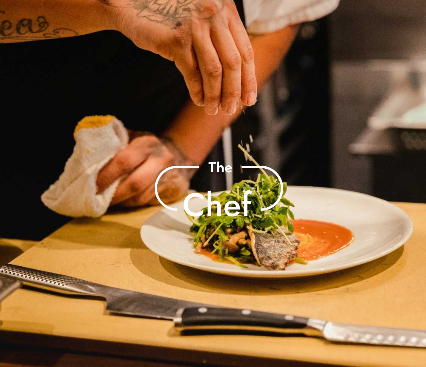 Chef's hand adding garnish to a plate with seared meat and salad topped over a splash of red sauce. On it the title "The chef"