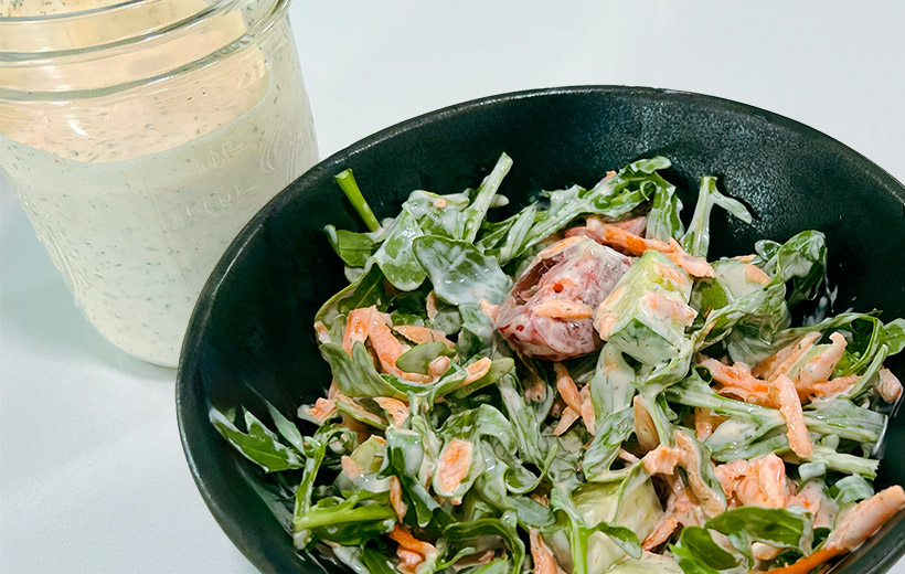 black bowl with mixed salad greens, tomato and carrots with ranch dressing. on the side, a jar with homemade ranch dressing.