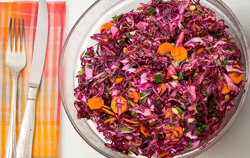 A large bowl with a beautiful mediterranean red cabbage slaw. with sliced carrots, parsley, and roasted nuts.