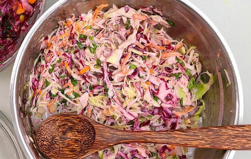 a large bowl with classic coleslaw. Green and red cabbage mixed with carrots scallions and parsley with a delicious mayo-based dressing.